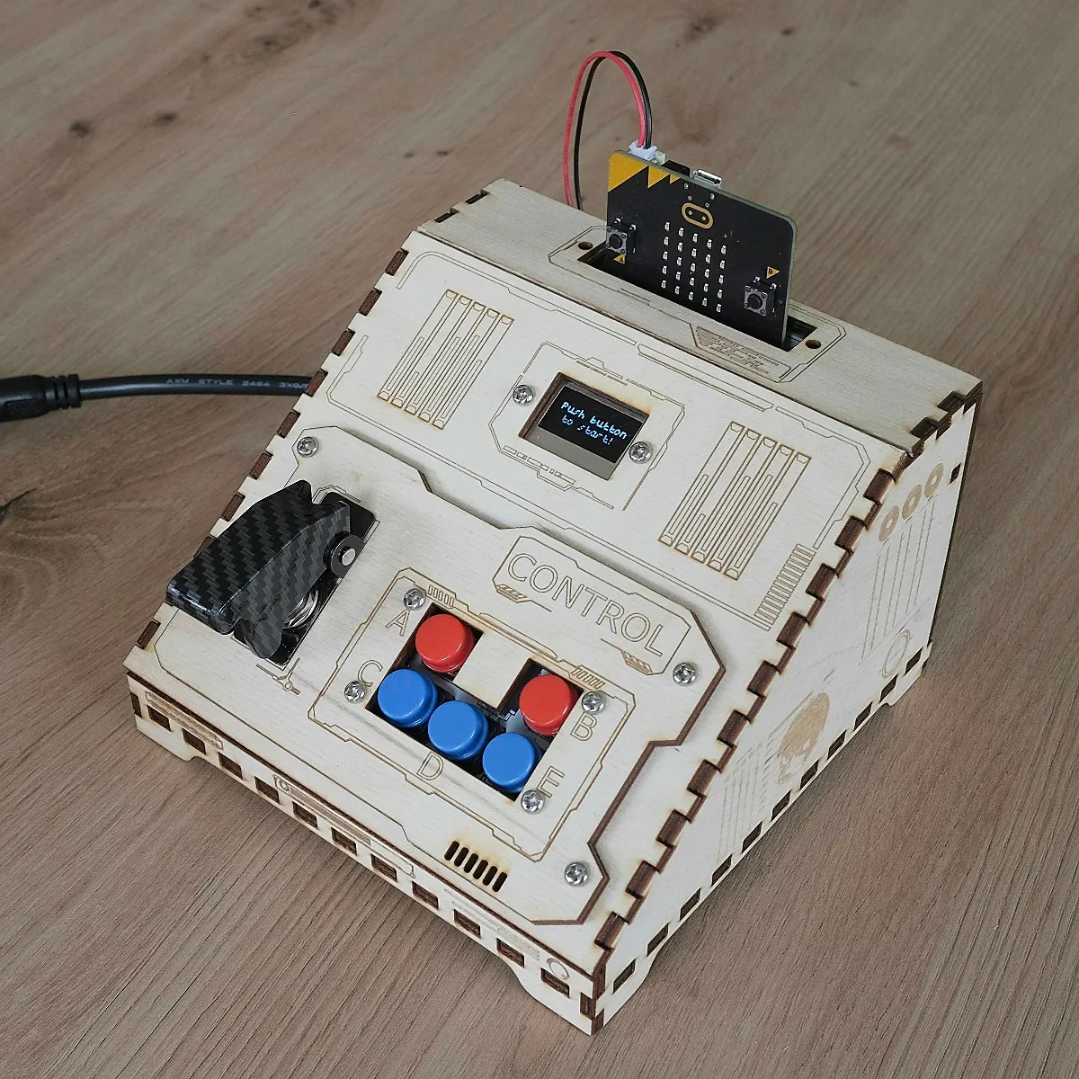 The Control console: a laser cut wooden box with a micro:bit, an OLED screen reading "Push button to start!", a covered flick switch and five coloured push buttons.