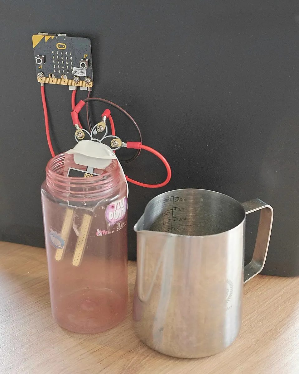 The fuel tank: a plastic bottle with a moisture sensor taped inside, wired to a micro:bit, next to a metal jug.