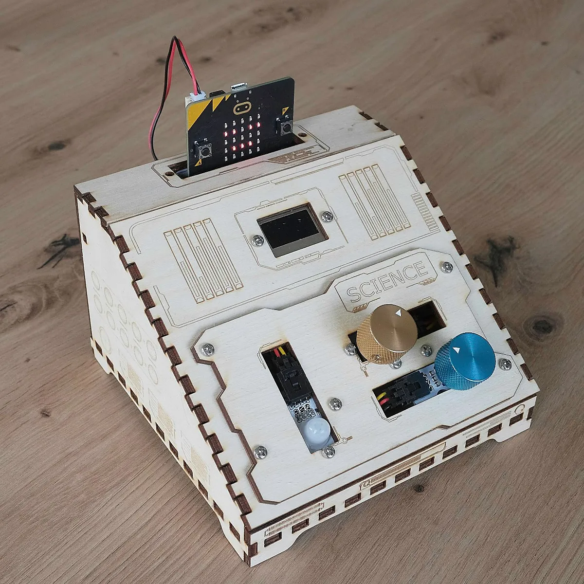 The Science console: a laser cut wooden box with a micro:bit slotted in the top, a small OLED screen, a gold and a blue dial, and a motion sensor.